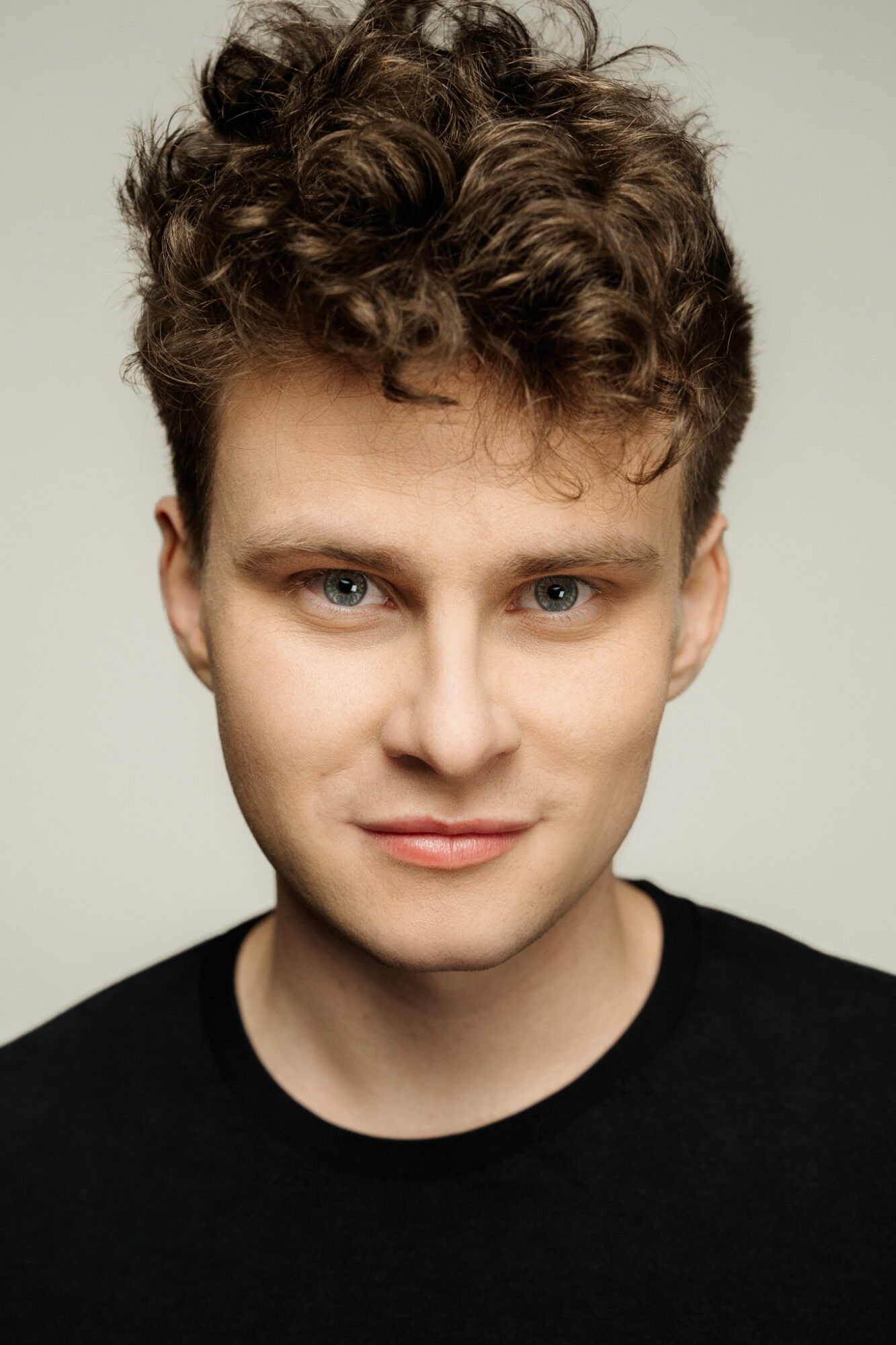 Portret mężczyzny. Boki krótko przystrzyżone, na górze burza loków. Brwi jasne, oczy niebieskie. Usta wąskie, układają się w uśmiech.